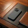 Black phone case on a wooden desk with a lamp and notebook.