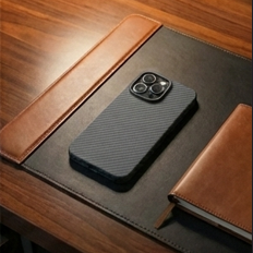 Black phone case on a wooden desk with a lamp and notebook.